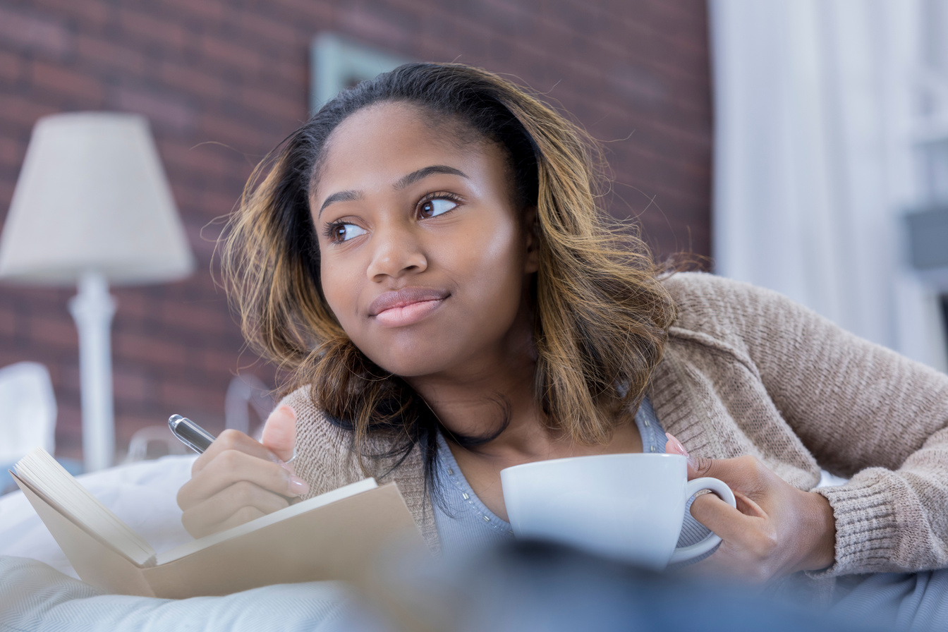 African American woman daydreams while writing in journal